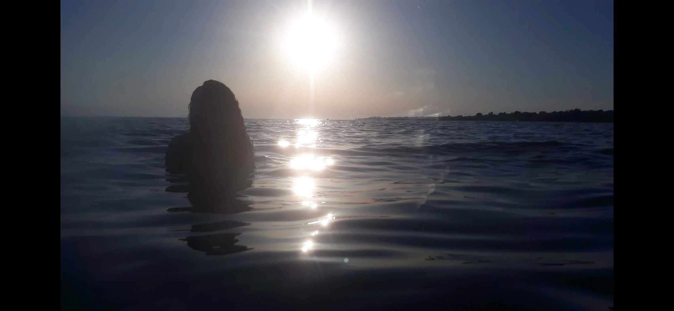 Silhouette figure standing in ocean at golden hour